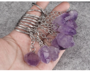 Close-up of raw amethyst crystal keychains held in hand showing natural mineral texture