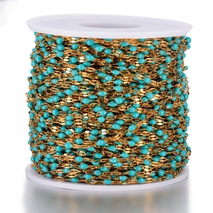 Detail of DIY golden stainless steel chain with blue enamel beads on a white spool