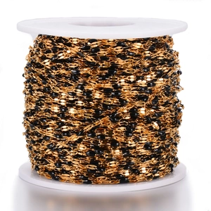 Macro shot of gold-plated stainless steel chain with black enamel beads on a white spool