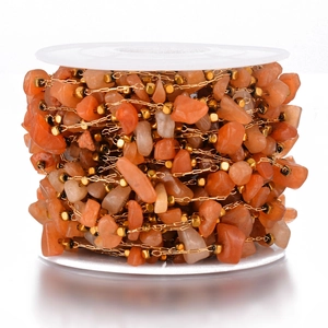 Close-up of orange crushed stones and gold beads on a spool for DIY jewelry making