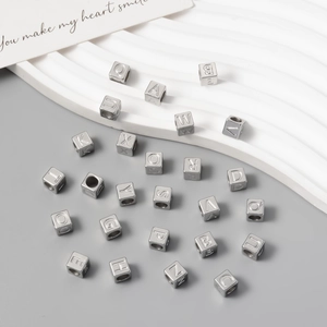 Macro view of polished silver square alphabet beads with engraved letters for DIY necklaces