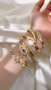 Detailed view of gold snake and evil eye bracelets with crystal inlay and shell accents