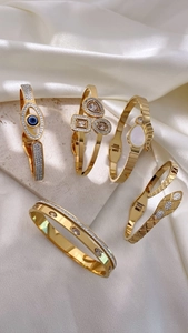 Detail of five gold bracelets featuring evil eye and geometric charms on silk and stone
