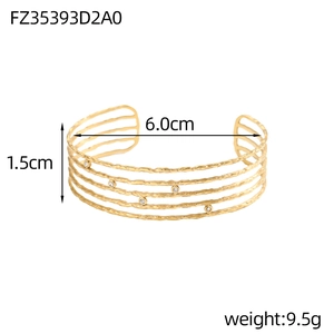 Dettaglio di un bracciale a polsino dorato con texture a strati e pietre di zircone
