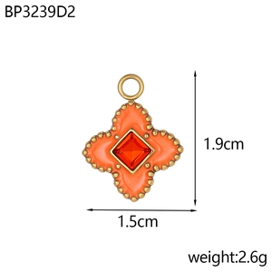 Détail d'un pendentif trèfle en émail orange avec gemme rouge et bordure perlée dorée