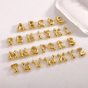 Macro shot of 26 puffed gold alphabet pendants arranged on a white textured surface