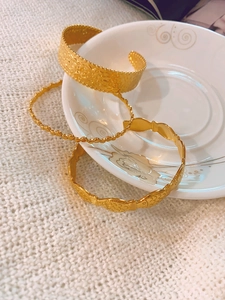 Close-up of golden hammered cuff and textured bangle bracelets set on ceramic plate