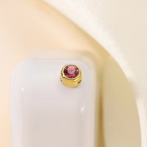 Detailed macro view of a gold-plated circular charm with a pink cubic zirconia stone