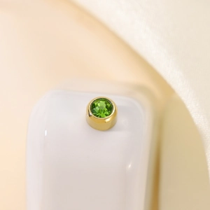 Macro shot of circular green gemstone stud earring with gold bezel setting and faceted cut