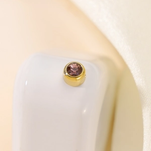 Macro shot of gold pendant with a faceted magenta zircon stone on white silk cloth