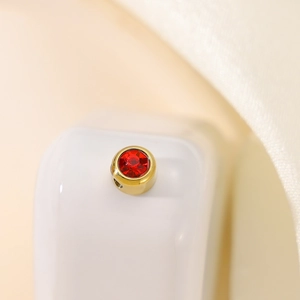 Macro shot of gold-plated round pendant with inlaid red crystal and side hole detail