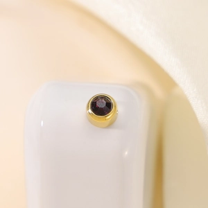 Macro detail of gold-plated circular stud earring with bezel-set deep red gemstone