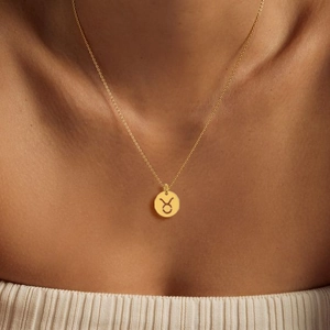 Lifestyle shot of a polished gold Taurus zodiac pendant on a fine necklace chain