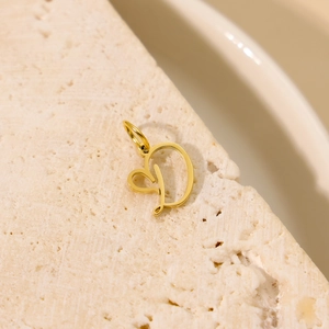 Détail d'un pendentif cœur avec lettre D dorée posé sur une texture en pierre