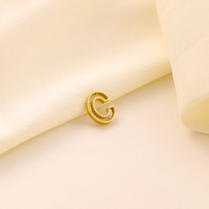 Détail macro d'un pendentif lettre C doré évidé sur un tissu plissé crème élégant