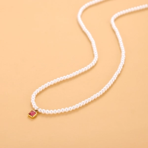 Primer plano de collar de perlas con colgante cuadrado dorado y gema de rubí rojo