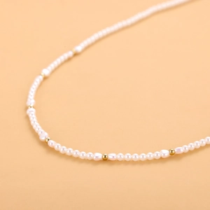 Primer plano de perlas blancas y cuentas doradas en un collar de lujo estilo francés