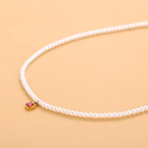 Primer plano de collar de perlas con colgante cuadrado de gema roja y borde dorado