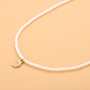 Detalle de collar de perlas con colgante de luna creciente dorada y cristales brillantes