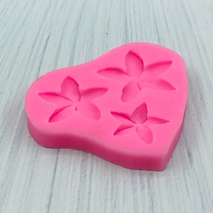 Pink silicone mold for chocolate flowers with three frangipani shapes on wood surface