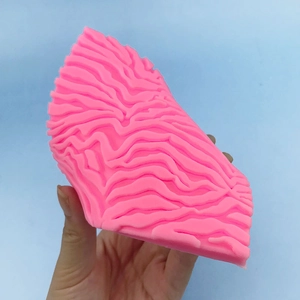 Pink silicone cleansing brush with wavy texture pattern shown against a blue background