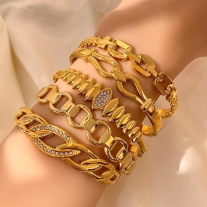 Dettaglio di bracciali dorati sovrapposti con pavé di cristalli e nodo intrecciato