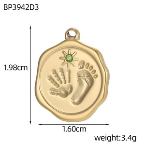 Macro detail of a gold coin pendant with handprints, footprints and green sun gemstone