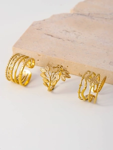 Detail of three gold rings featuring leaf, floral, and geometric cutout designs on stone