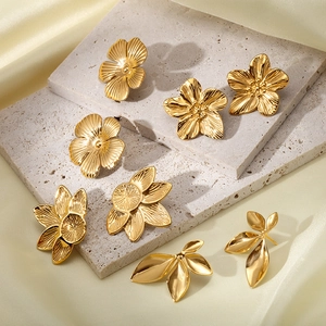 Elegant gold flower and leaf stud earrings set on a grey stone tray background