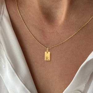 Detail of a gold rectangular letter R pendant necklace worn on a female model