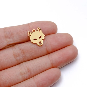Vue rapprochée d'un pendentif tête de loup en acier doré tenu par la main pour taille