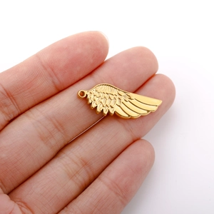 Detail view of golden angel wing pendant on palm showing 2-3cm actual size and texture