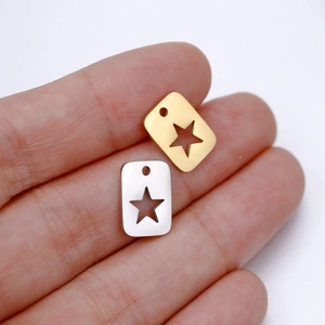 Macro view of small rectangular star pendants in gold and silver on a finger for DIY jewelry