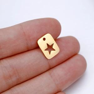 Close-up of golden rectangular charm with star cutout held between fingers for scale