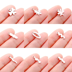 Various mini stainless steel leaf and wave charms for DIY jewelry making displayed on fingertip