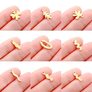 Macro detail of nine gold stainless steel leaf and wave charms held by fingers for scale