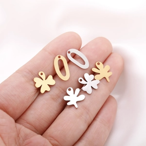 Detailed view of gold and silver clover and leaf metal charms held in hand for scale