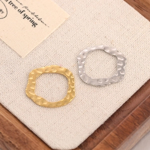 Golden and silver hammered wave pendants with irregular textured surface on linen