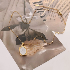 Detalle del collar de acero dorado con diseño de flores, cinta de Chanel y revista Vogue
