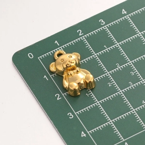 Macro shot of gold teddy bear charm on cutting mat showing its 20mm height scale