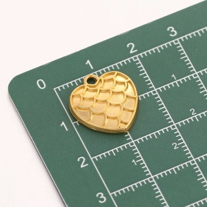 Macro shot of gold heart pendant with scale texture on a green measuring mat