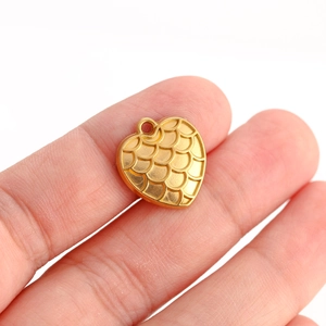 Detail of golden heart pendant with dragon scale texture shown on a fingertip