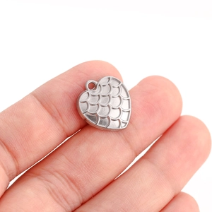 Macro shot of silver heart pendant with dragon scale texture held between fingers