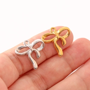 Colgantes de lazo en acero inoxidable oro y plata para joyería DIY mostrados en dedos