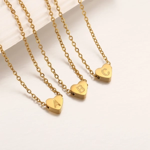 Detalle de tres colgantes de corazón dorados con letras A, B y C en cadenas de eslabones