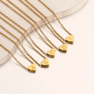 Detalle de cinco collares de corazón dorado con iniciales A-E sobre elegante soporte