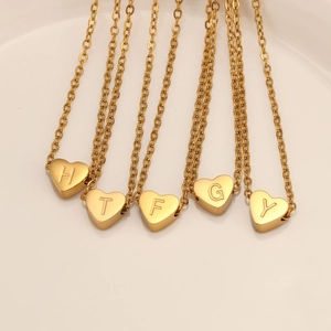 Primer plano de cinco collares de corazón dorados con letras H, T, F, G, Y y cadena clásica