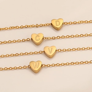 Detalle de cuatro collares dorados con colgantes de corazón y letras grabadas D C V W