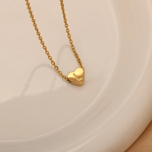 Primer plano de collar dorado con colgante de corazón y letra L en plato cerámico