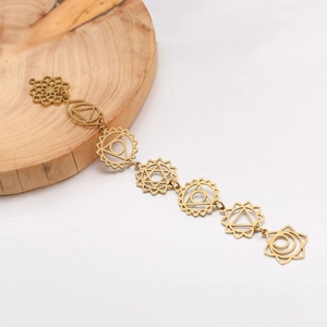 Gold stainless steel Seven Chakra lotus charm bracelet displayed on a natural wood slice